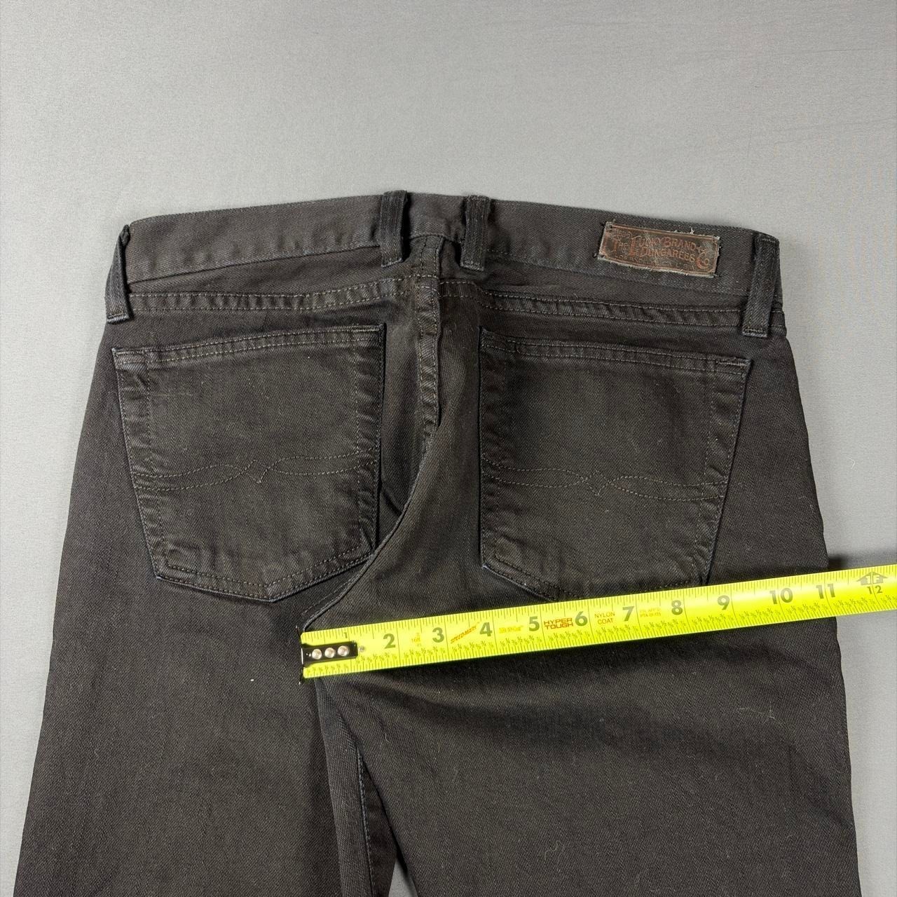 Black faded bootcut jeans with back pocket stitching and brown leather patch on waistband, measured against yellow tape.