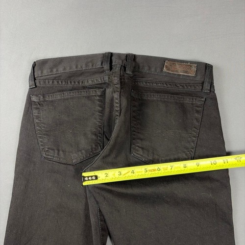 Black faded bootcut jeans with back pocket stitching and brown leather patch on waistband, measured against yellow tape.