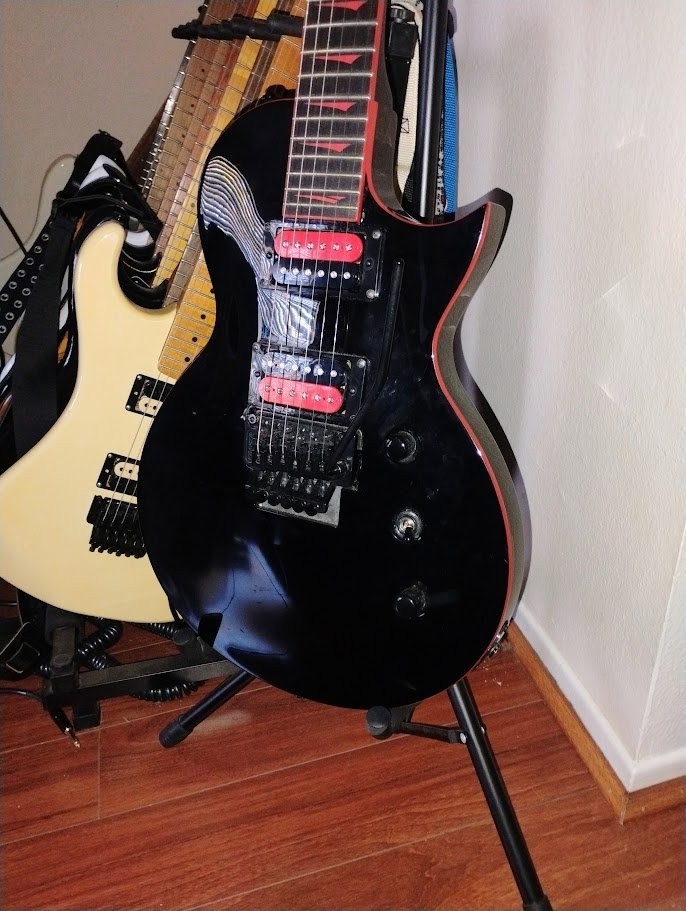 Black 2022 Kramer Assault electric guitar with white body, Floyd Rose bridge, coil tap, and red fret markers on stand.