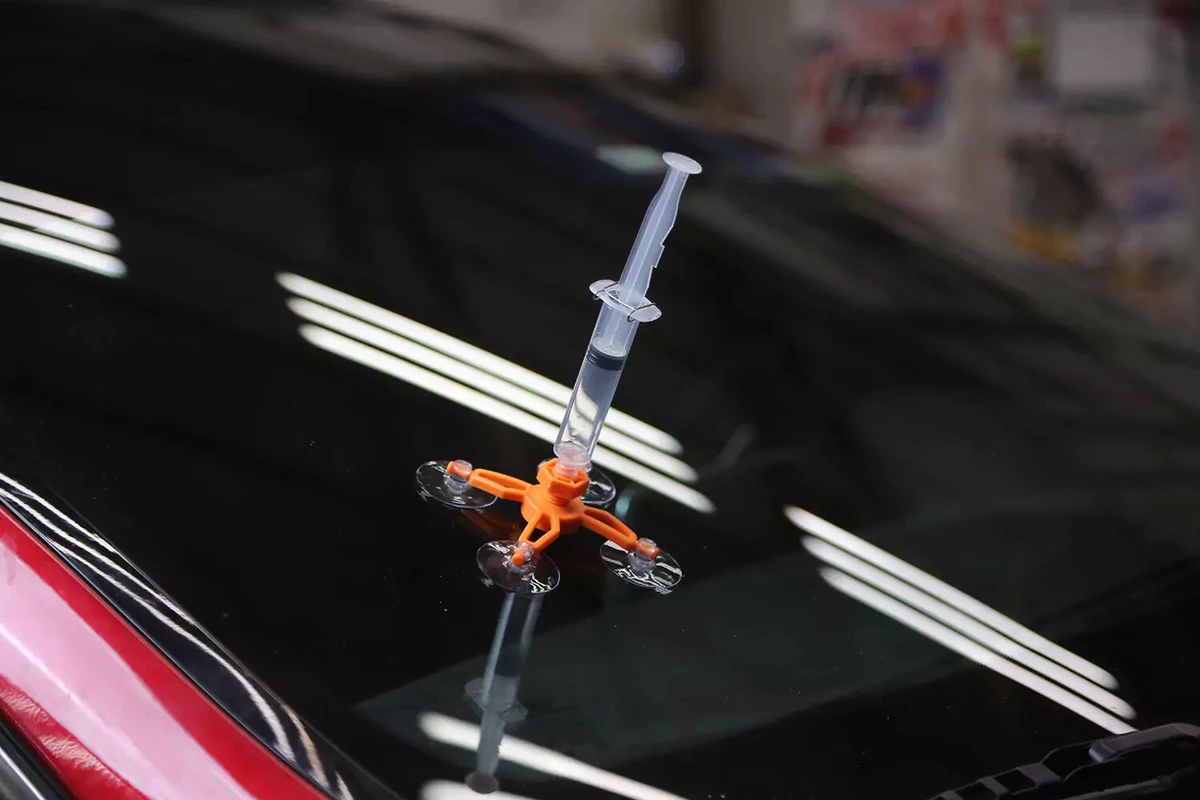 A syringe with its plunger pulled back creating a vacuum inside the repair jig of a windshield repair kit.