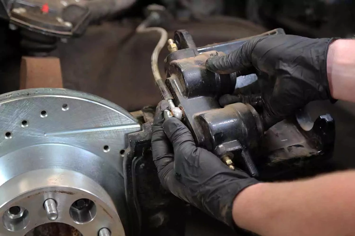 A mechanic loosening the brake fluid line’s banjo bolt by hand.