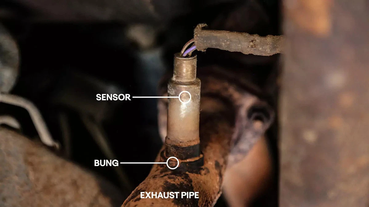 The original oxygen sensor screwed into its exhaust pipe bung behind the exhaust manifold.
