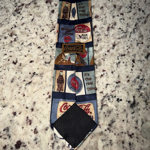 Blue necktie with vintage red and white Coca Cola ads, cartoon panels, and white “It’s the real thing” text.