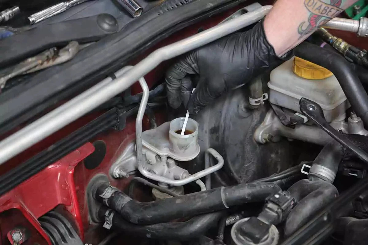 A mechanic wearing black nitrile gloves, dips a test strip into the clutch fluid reservoir.