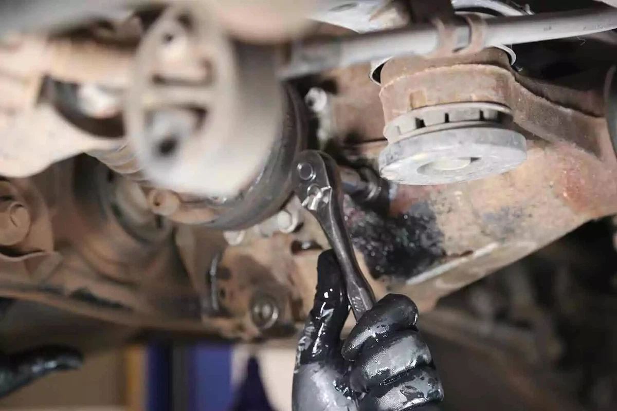 A mechanic wearing a black glove uses a ratchet to close the fill plug of a vehicle's rear differential.