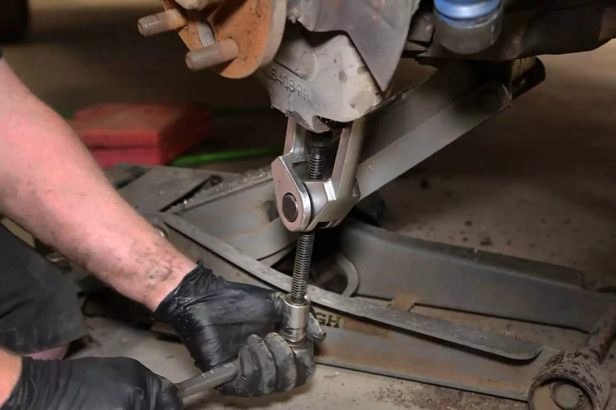 A mechanic uses a separator tool to remove the pin from the knuckle.