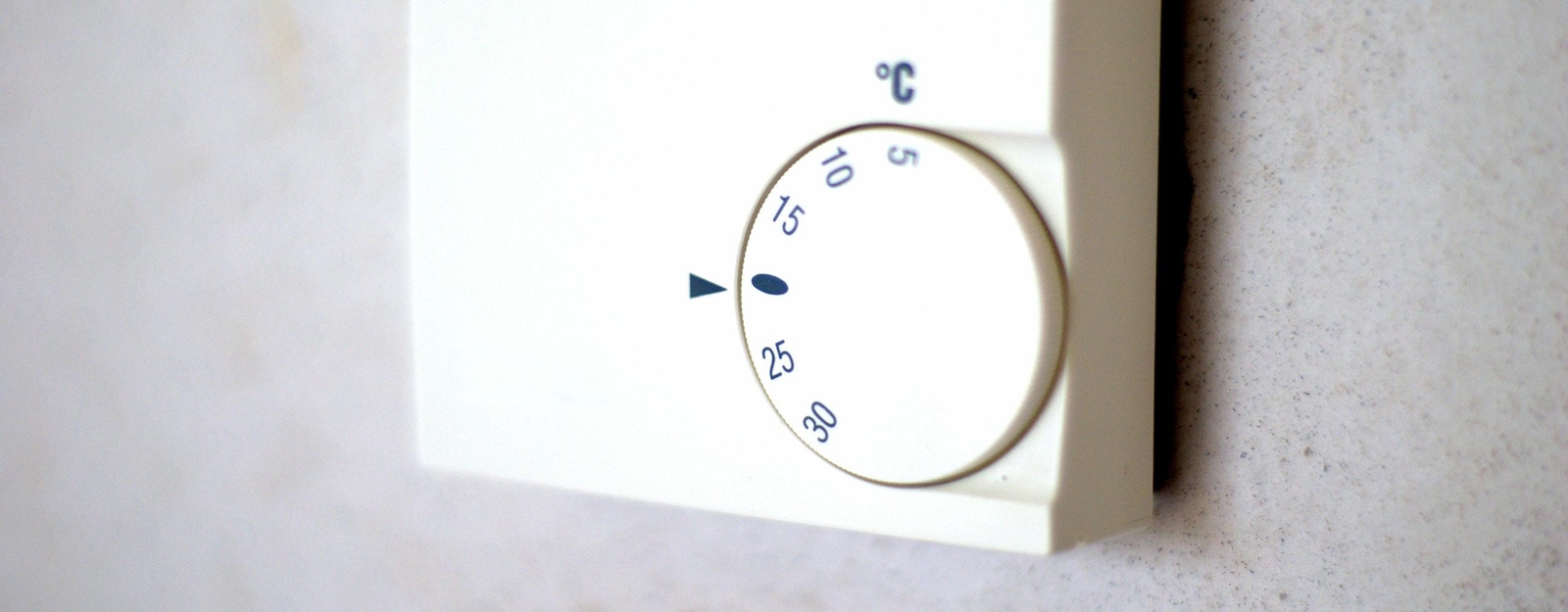 Ein Raumthermostat, das an einer Wand befestigt ist und mit dem man die Temperatur von 5 bis 30 Grad Celsius einstellen kann