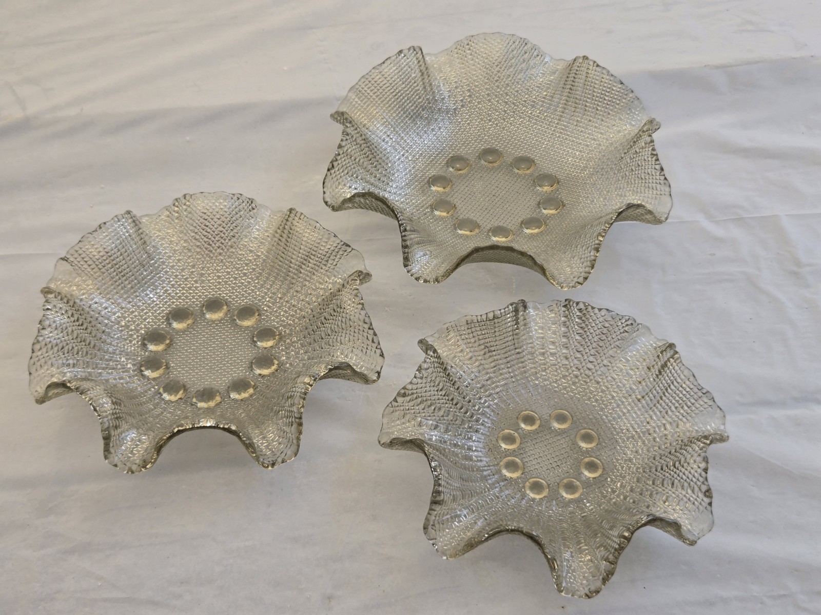 Set of three grey smoked glass nesting bowls with ruffled rims on a white background.