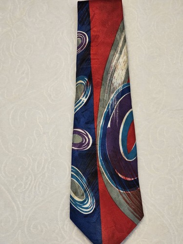 Red necktie with blue and gray abstract swirl pattern, silver buttons, and “Made in U.S.A.” label on white surface.