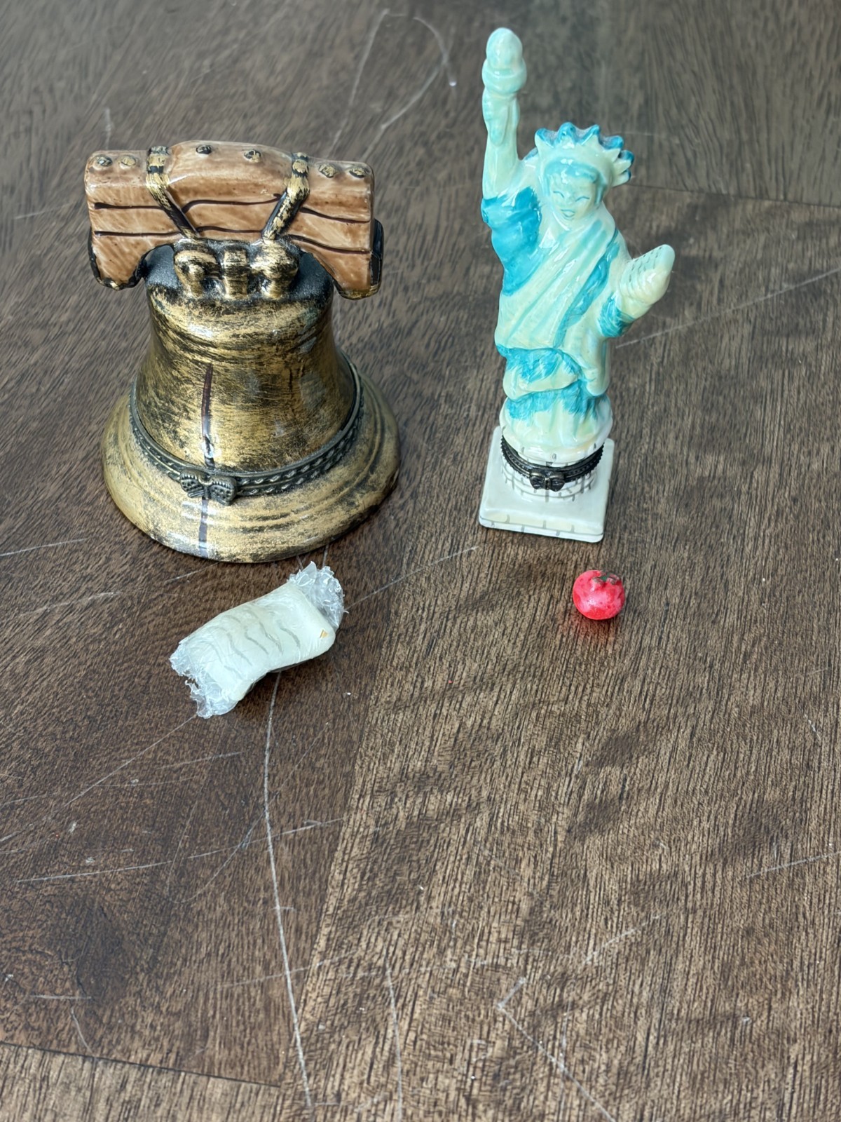 Miniature Liberty Bell with gold accents beside a red, white, and blue Statue of Liberty figure on a wooden surface.