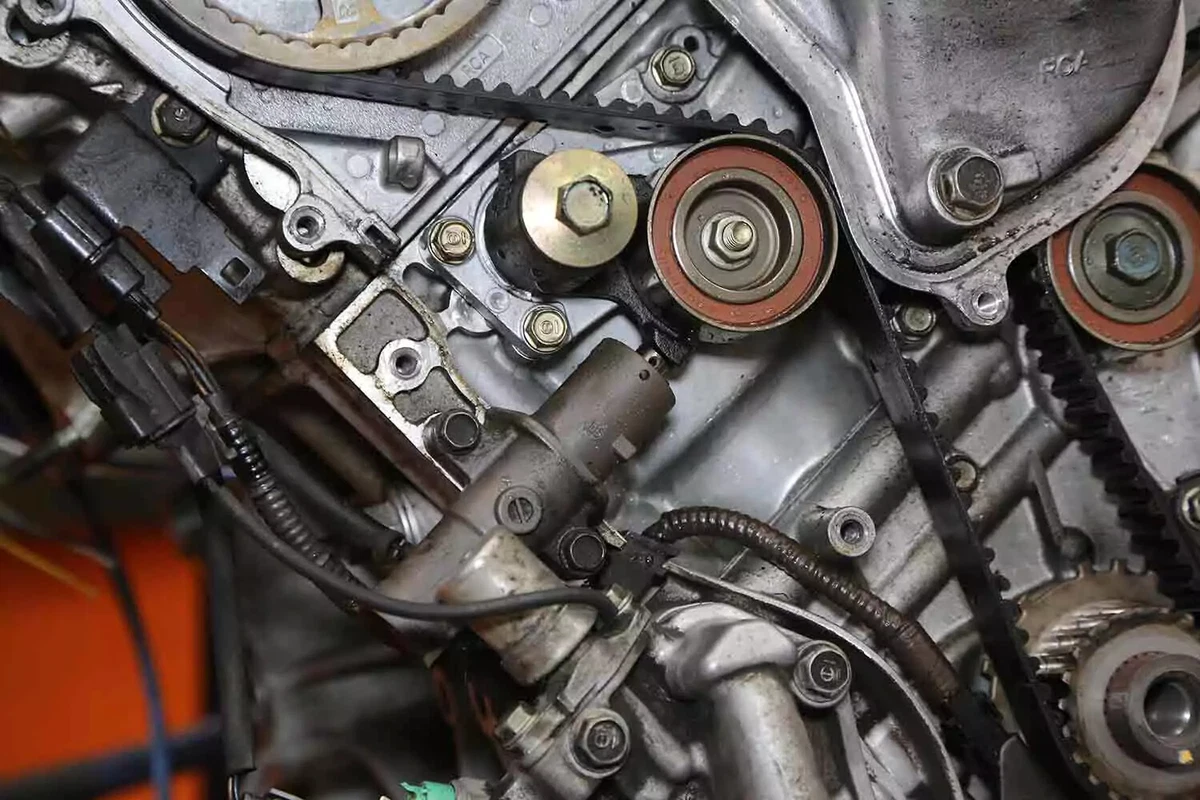 A mechanic wearing blue nitrile gloves points out the top-dead-center alignment mark on a timing belt gear with his left index finger.