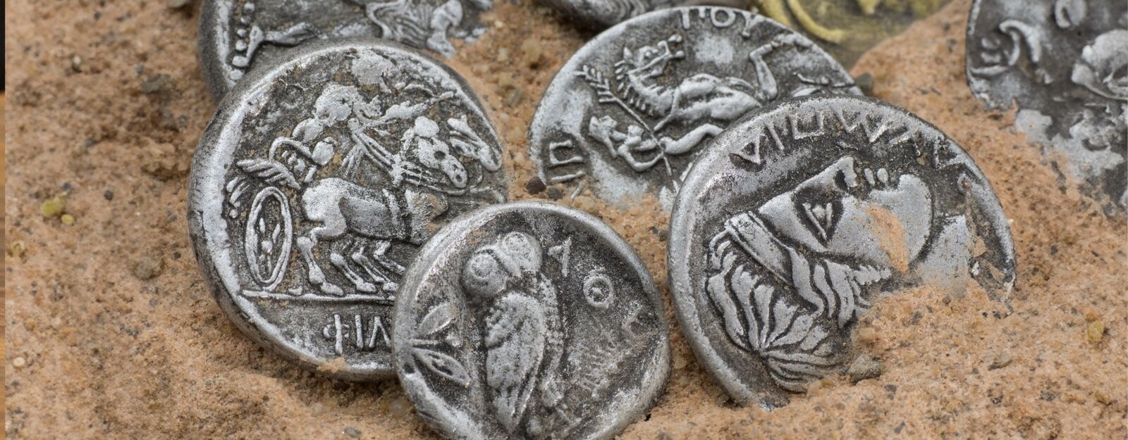 Nahaufnahme von alten griechischen Münzen, die willkürlich verteilt im Sand liegen
