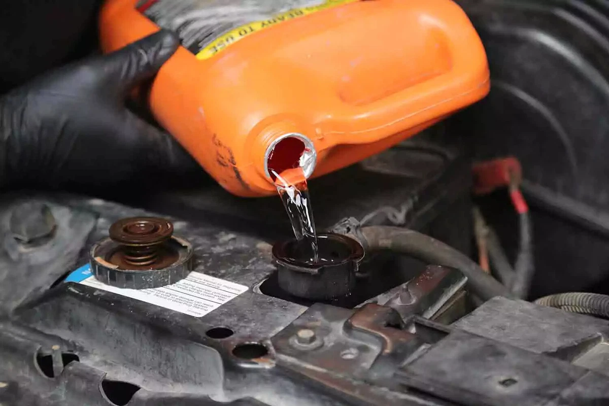 A mechanic pours new coolant fluid from an orange container into the radiator.