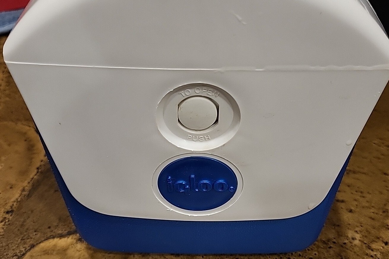 White rectangular Igloo cooler with black top, blue side panel, and white circular opening button.