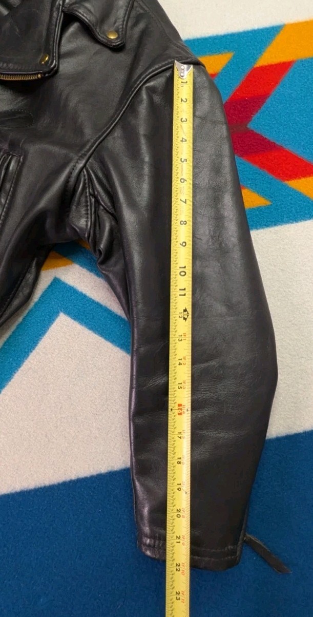 Black vintage leather Langlitz motorcycle jacket with yellow measuring tape showing sleeve length and Portland Made In USA size 46.