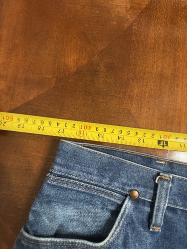 Blue vintage Wrangler jeans size 36x30 with yellow measuring tape across the waistband, showing front pockets and button closure.