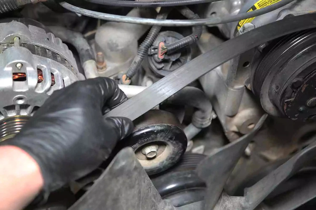 A mechanic wearing a black glove removes the serpentine belt from the tensioner.