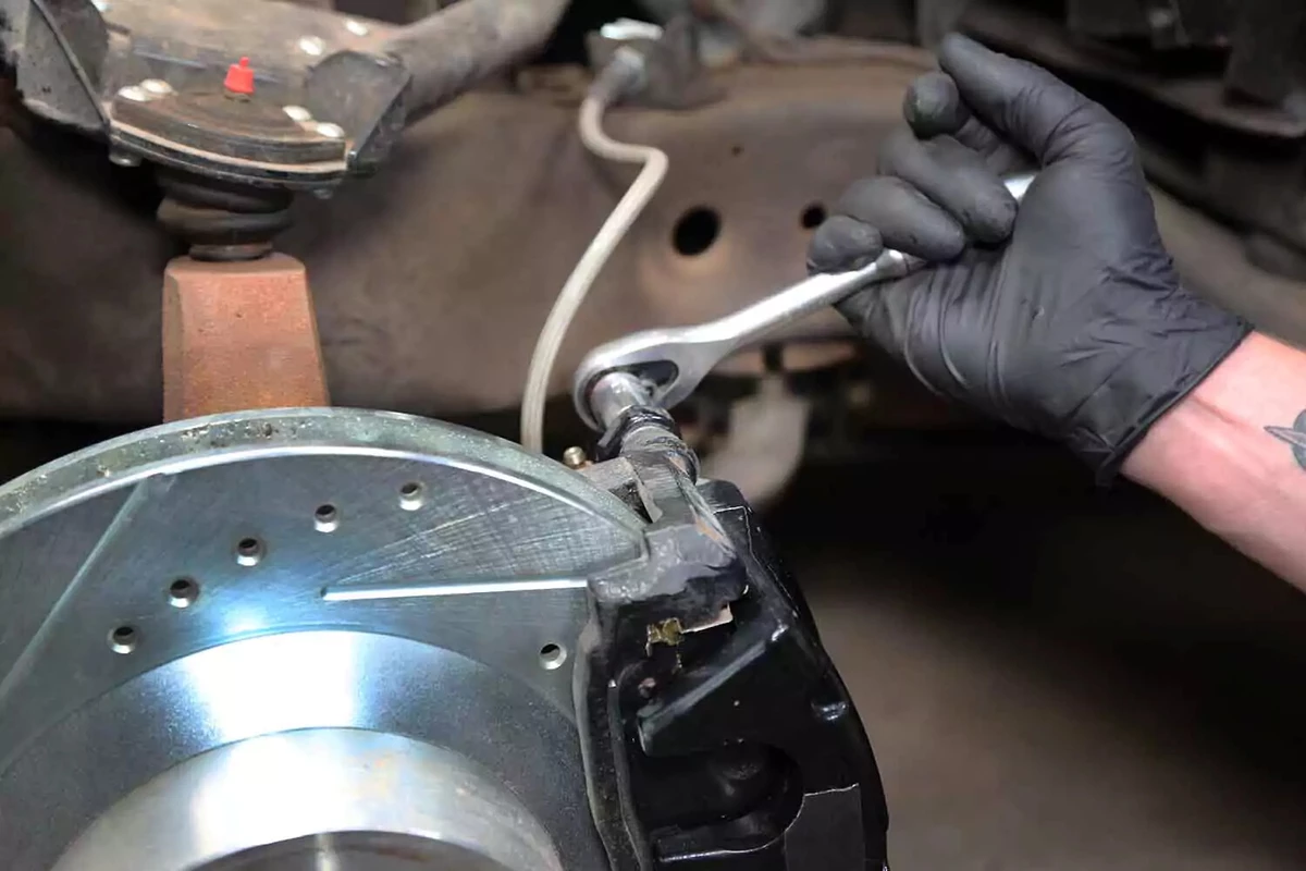 A mechanic tightens the brake caliper bolt with a ratchet wrench.
