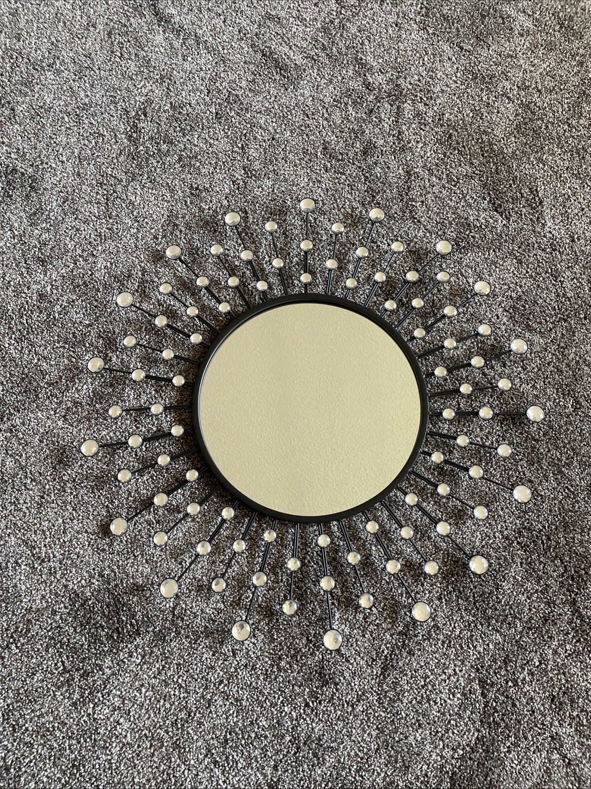 Round mid-century starburst wall mirror with black metal rays tipped in silver beads, framing a round mirror.