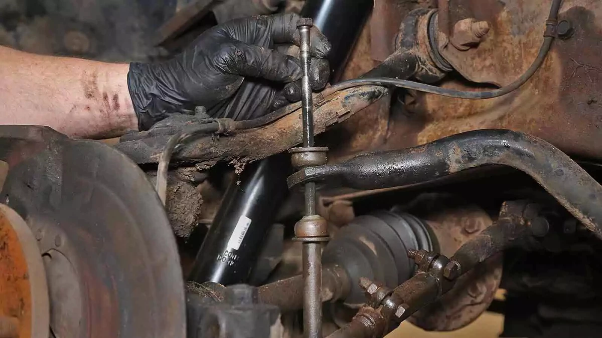A mechanic wearing a black nitrile glove in the process of removing a worn out sway bar link.