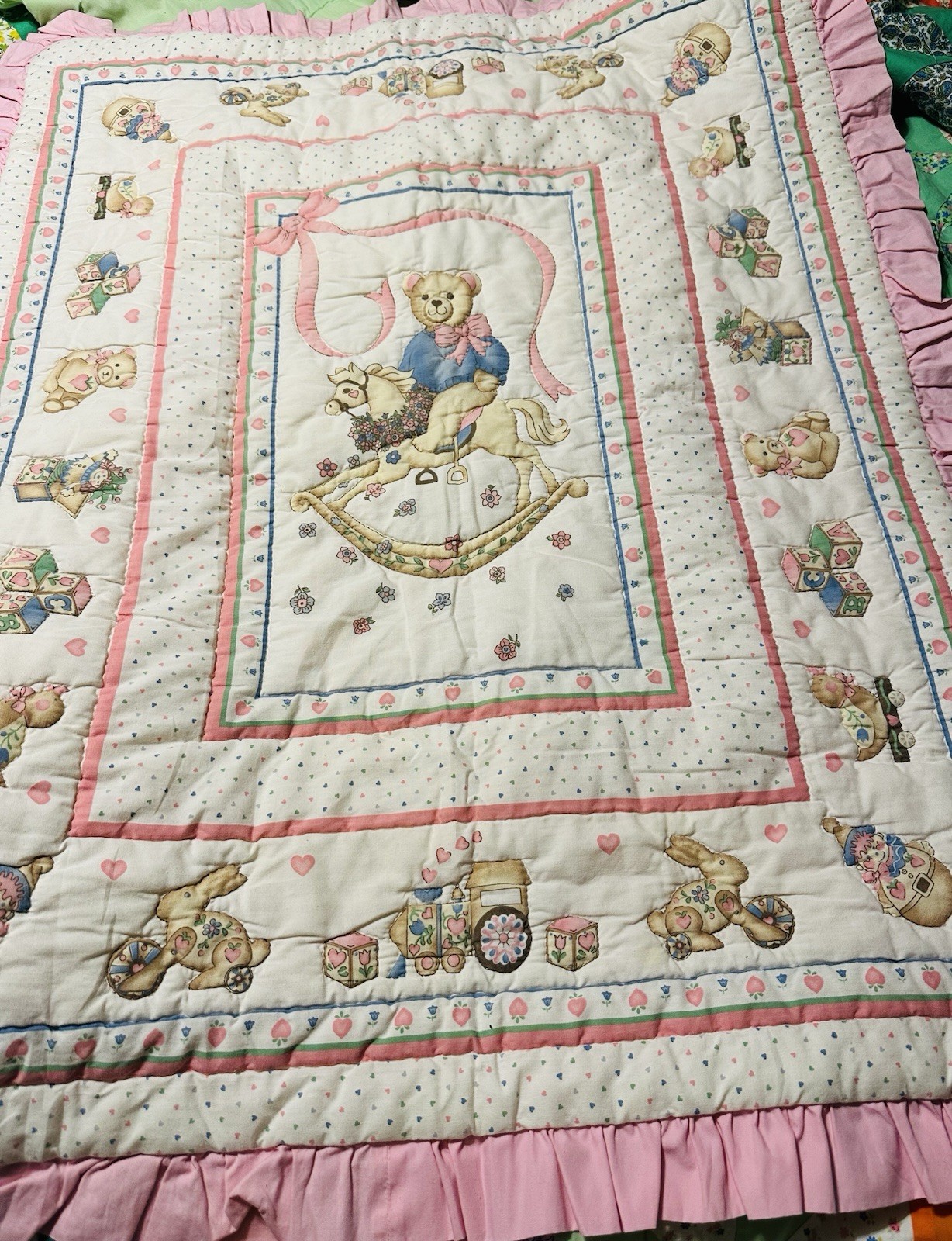 A vintage baby quilt featuring teddy bears, bunnies, and toys.