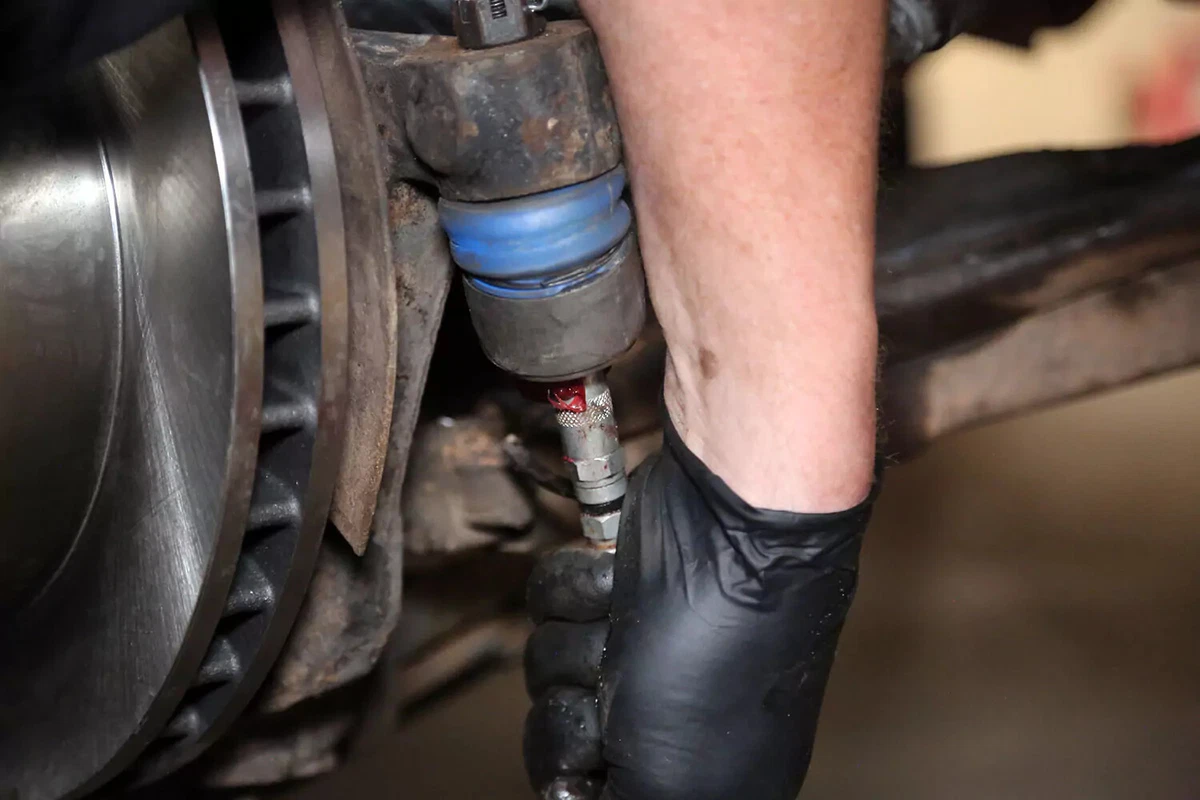 A mechanic fills a tie rod end with grease.
