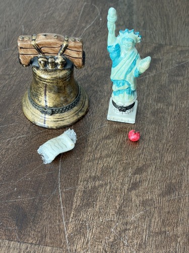 Miniature Liberty Bell with gold accents and matching Statue of Liberty figure, displayed on a wooden surface with red marble.