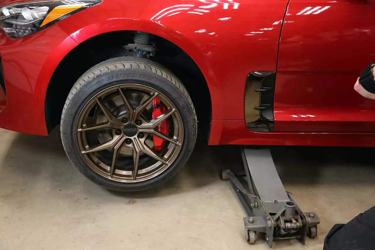 A car lifted using a floor jack, with its left front wheel off the ground.