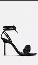 Elegant black heeled sandals. They feature a stylish floral detail.