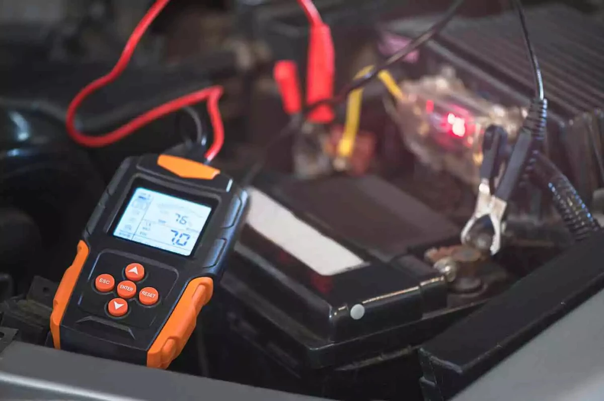 An orange and black multimeter attached to a car battery.