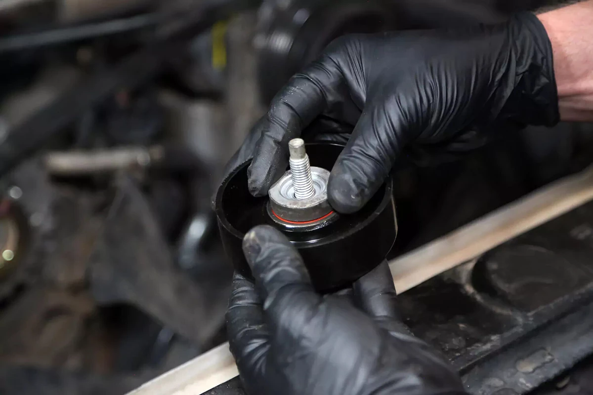A mechanic assembles the new idler pulley with the original bolt and spacer.