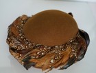 Brown hat with 100% wool base, topped with tan and brown feathers patterned with black eyes and beaks.