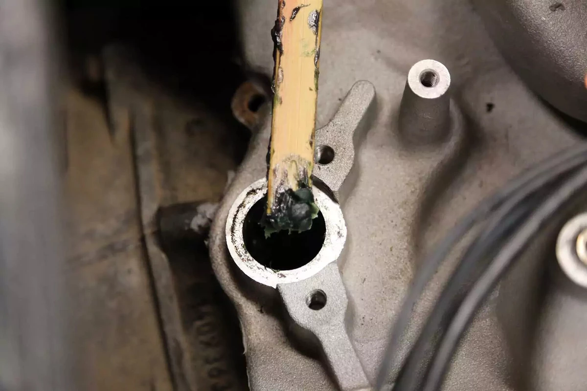 A mechanic inserts engine-assembly paste into the engine using a paint stick to keep the oil pump shaft centered in the bore.