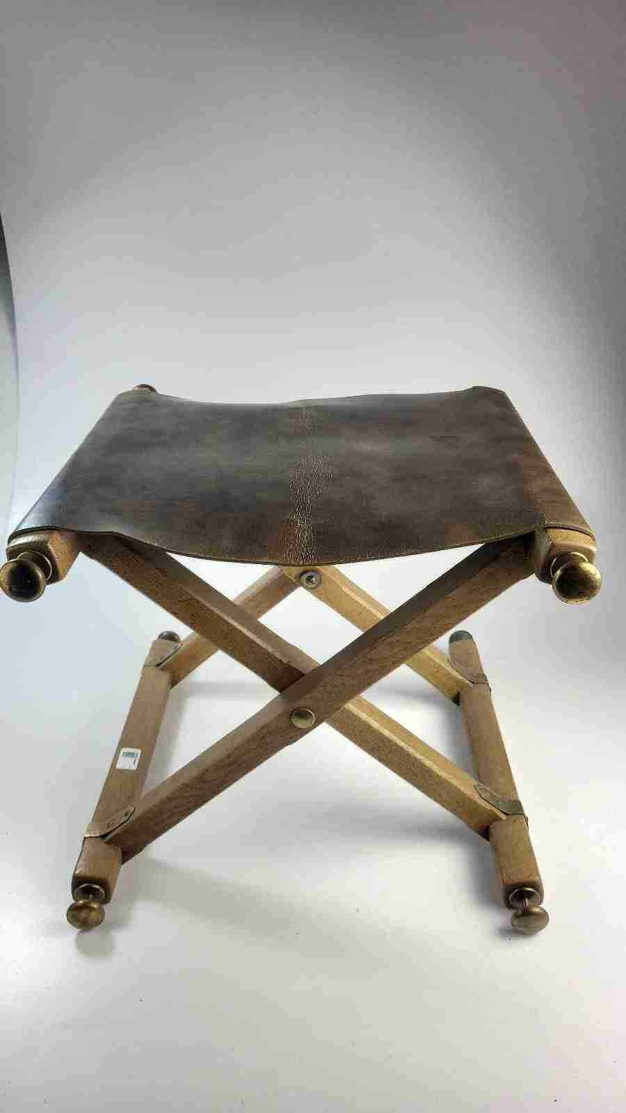 A folding stool with an oak frame, brass hardware, and a leather sling seat.