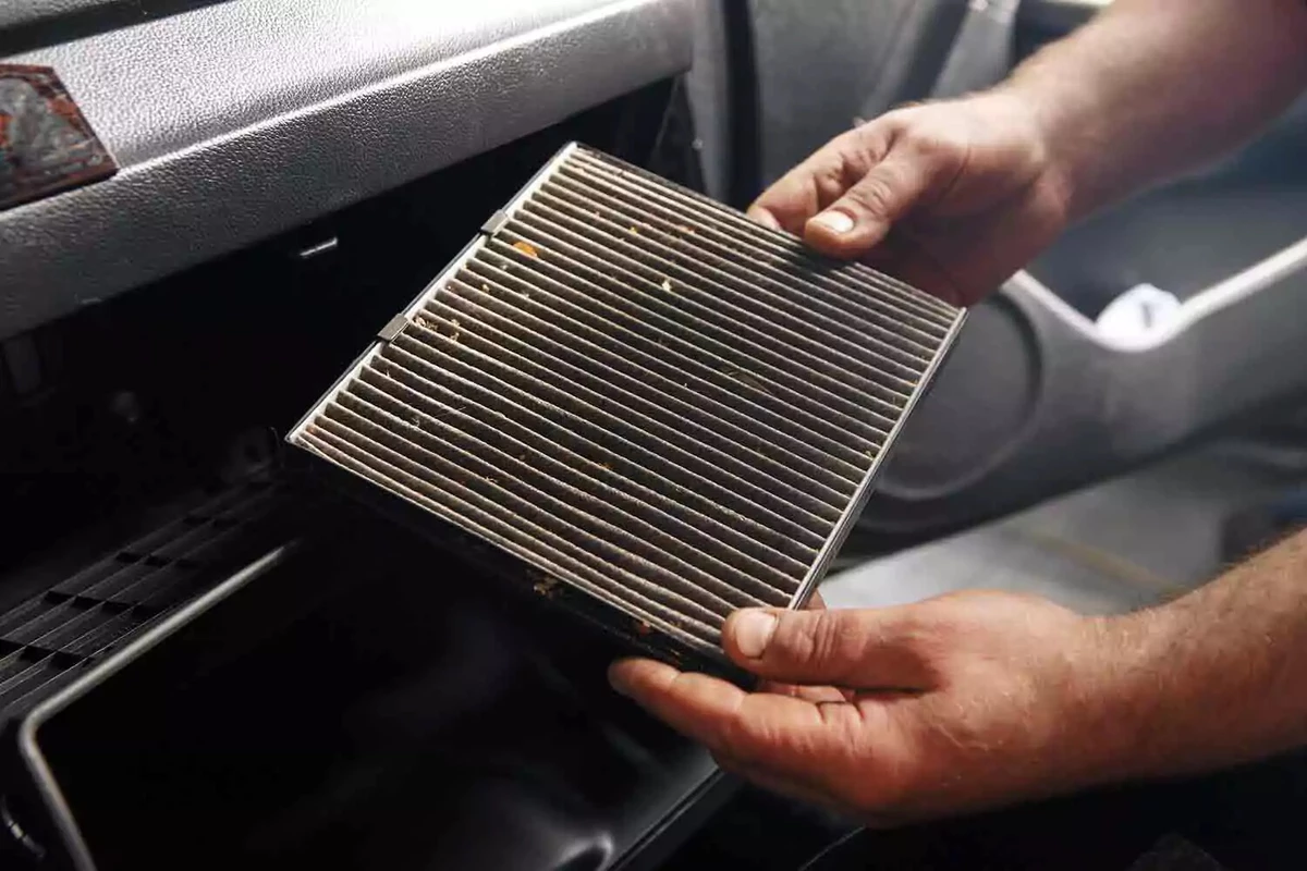 A driver examines a dirty cabin air filter after removing it.