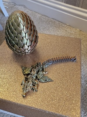 3D-gedruckter geflügelter Gelenkdrache und gold/kupferfarbenes Ei