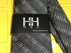 Navy blue neck tie with diagonal white stripes, black tag reading “H&H men” and “100% silk stain resistant” in bold black letters.