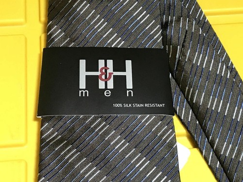 Navy blue neck tie with diagonal white stripes, black tag reading “H&H men” and “100% silk stain resistant” in bold black letters.
