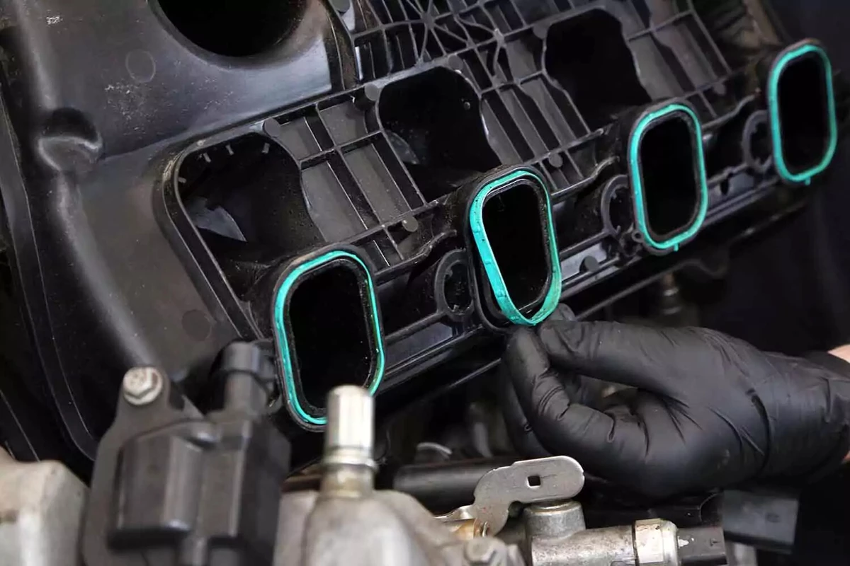 A mechanic replacing the silicone gaskets on a plastic intake manifold base.