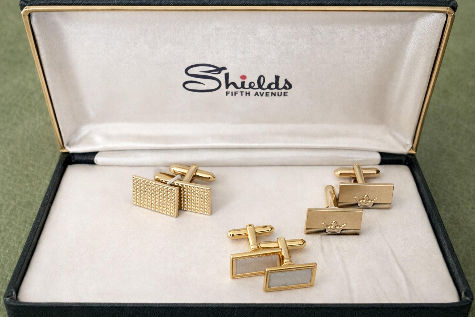 Three pairs of gold-tone cufflinks in their original box on a white background.