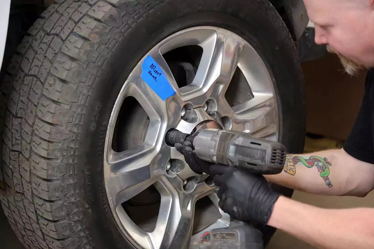 A mechanic removing a lug nut on a pickup truck tire using an impact wrench.