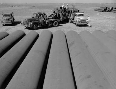Three trucks, largest loaded sections pipe, while foreground domin Old Photo