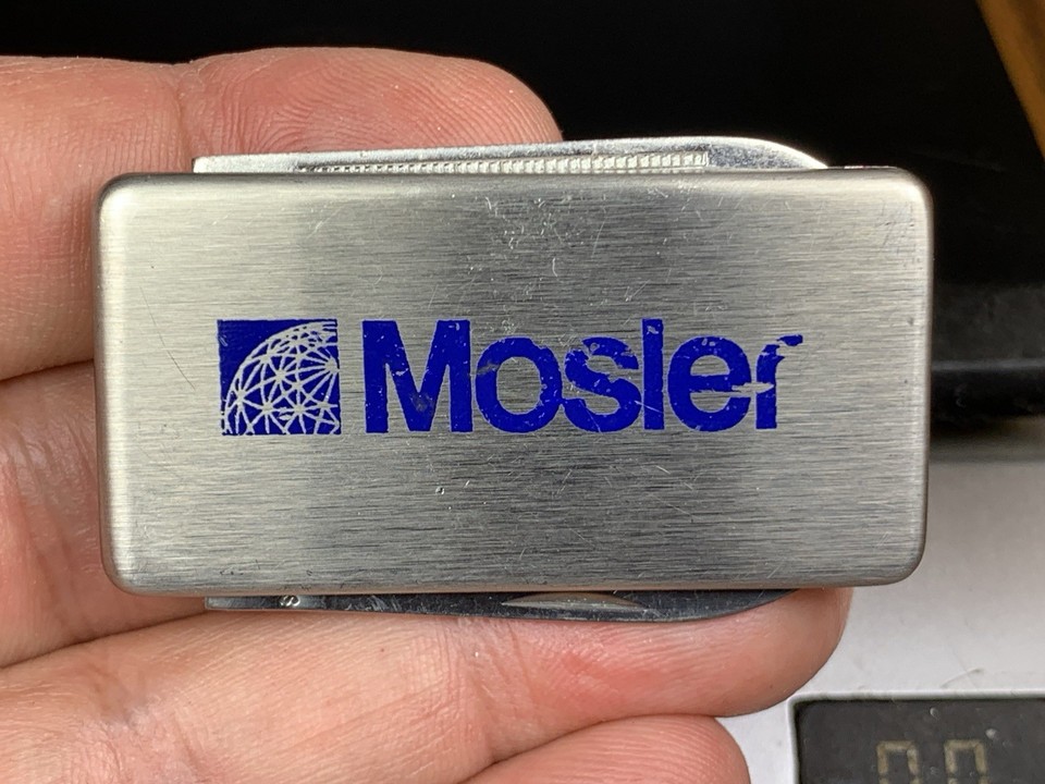 A stainless steel money clip with a built-in knife and file bearing the MOSLER Co logo — a dead-serious piece of mid-century executive EDC that doubles as a conversation piece.