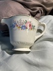 White ceramic pitcher with gold rim, blue and pink floral print, and “Made in U.S.A.” text on fabric background.