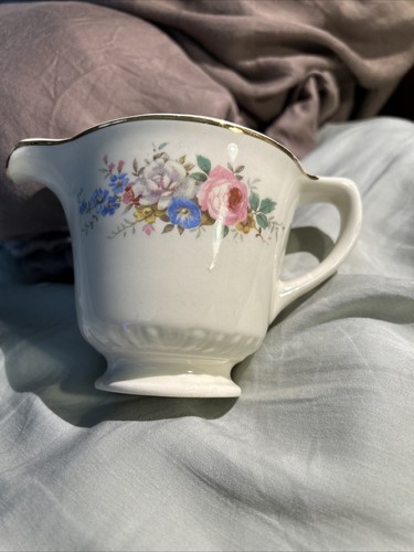 White ceramic pitcher with gold rim, blue and pink floral print, and “Made in U.S.A.” text on fabric background.