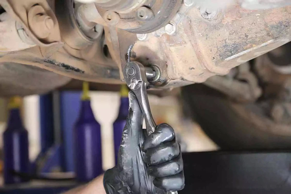 A mechanic wearing a black glove uses a socket to replace the drain plug of a vehicle's rear differential.