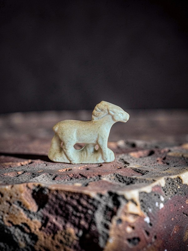 A small, carved stone animal figure, possibly a horse or ram.