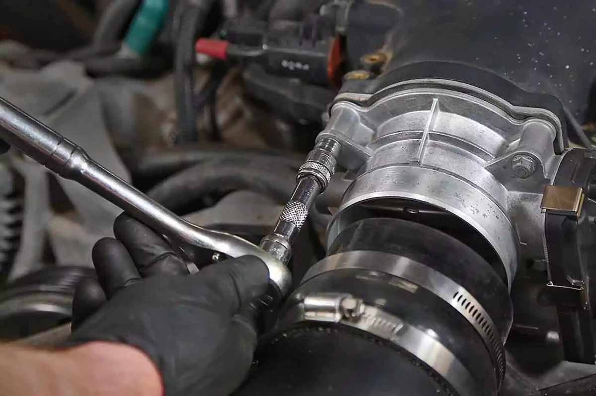 A mechanic wearing a black nitrile glove, tightening a bolt on a new throttle body, using a socket wrench with an extension.