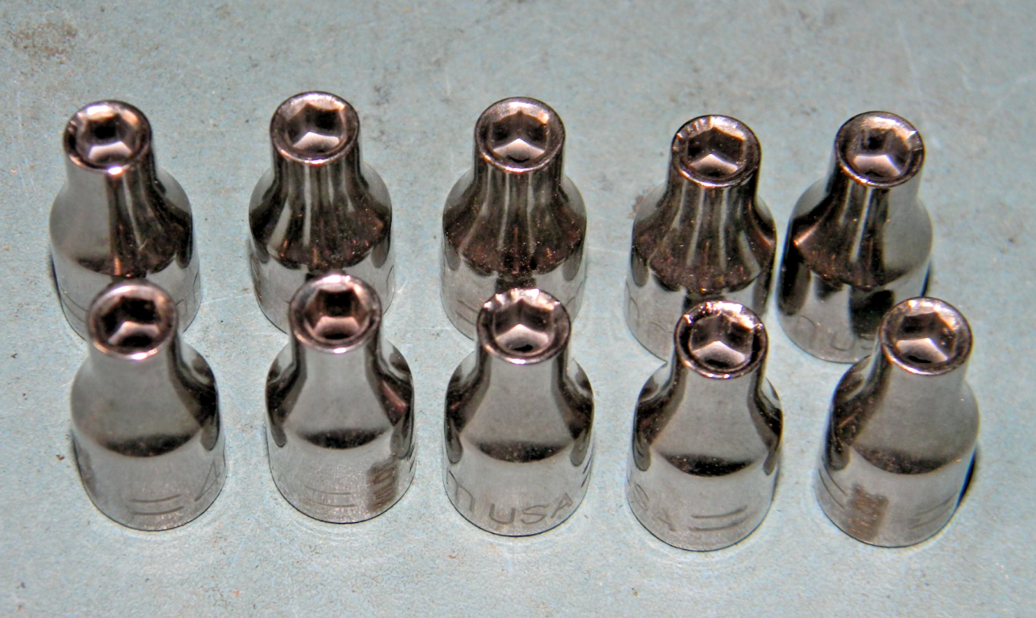 Fourteen silver 4mm socket 6 pt wrenches with black handles, arranged in a row on a light blue surface.