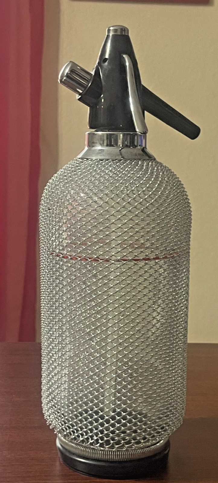 Chrome-and-mesh vintage soda siphon bottle with glass body.